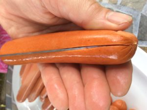 The hot dog is cut to length with one slice of the knife and placed open on the grill surface 