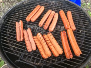 the dogs with the different slicing are placed on the charcoal grill with double filet wood pieces added for flavor. 